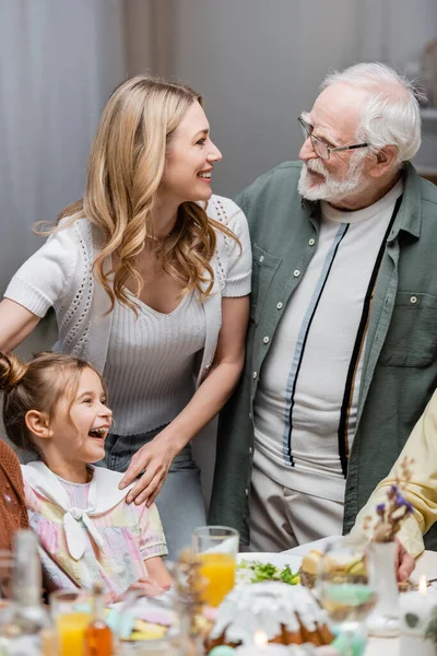 Femme heureuse parlant à père aîné près de rire fille pendant le dîner de Pâques — Photo de stock