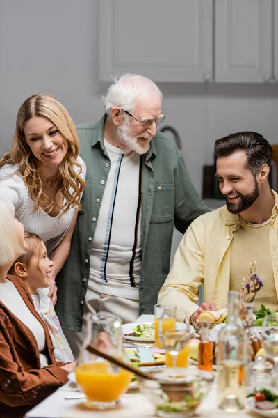 Familia feliz sonriendo cerca de la mesa servida con cena oriental - foto de stock