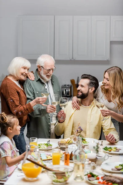 Glückliche Familie klimpert Weingläser neben Tisch serviert mit Osteressen — Stockfoto