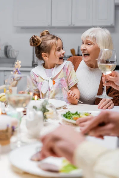 Взволнованная бабушка и девочка смотрят друг на друга и смеются во время пасхального ужина — стоковое фото