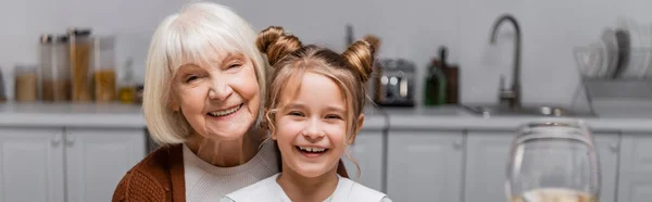 Fröhliche Seniorin mit Enkelin blickt in Küche in die Kamera, Transparent — Stockfoto