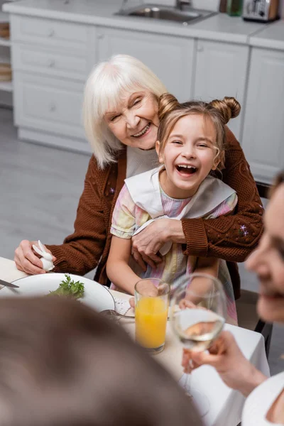 Happy senior woman embracing laughing granddaughter on blurred foreground — Stock Photo
