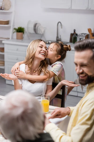 Preadolescente chica con los ojos cerrados besar feliz madre durante la cena festiva con la familia - foto de stock