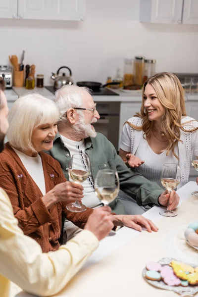 Femme heureuse parlant à des parents âgés tenant des verres avec du vin pendant le dîner de Pâques — Photo de stock