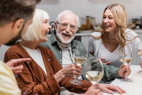 Homme flou pointant du doigt près de la famille joyeuse avec des verres à vin — Photo de stock