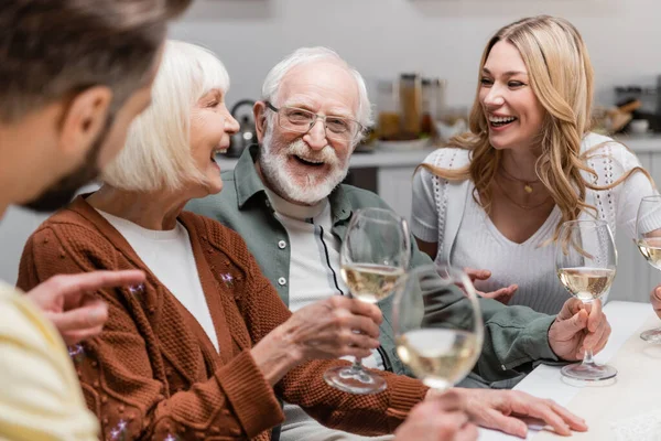 Hombre borroso señalando con el dedo cerca de la familia alegre con copas de vino - foto de stock