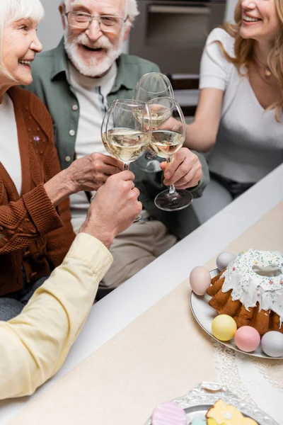 Pareja de ancianos tintineando copas de vino mientras celebran la Pascua con niños adultos - foto de stock