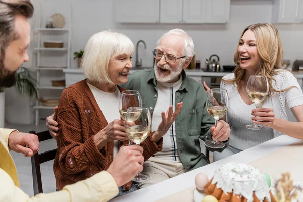 Senior woman holding glass of wine and laughing during family dinner — Stock Photo