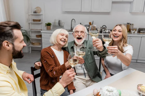 Alegre tostada familiar con copas de vino durante la celebración de Pascua en casa - foto de stock