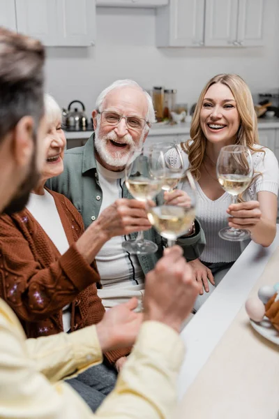 Padres ancianos felices tintineando copas de vino con hijo e hija adultos durante la celebración de Pascua - foto de stock