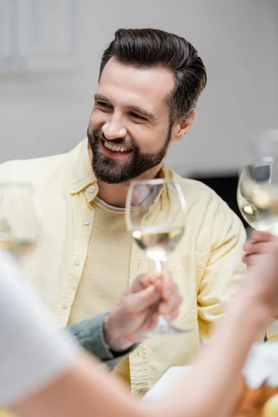 Hombre barbudo feliz sosteniendo copa de vino cerca de esposa borrosa durante la celebración de Pascua - foto de stock