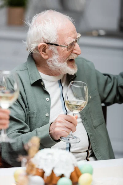 Веселый пожилой человек держит бокал вина во время празднования Пасхи с семьей — стоковое фото