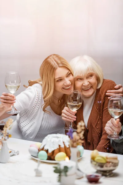 Mãe feliz e filha com copos de vinho abraçando durante o jantar de Páscoa — Fotografia de Stock