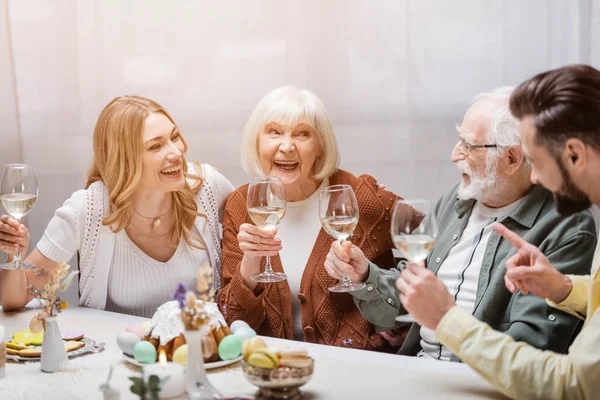 Homem apontando com o dedo perto de família feliz segurando copos de vinho durante o jantar festivo — Fotografia de Stock