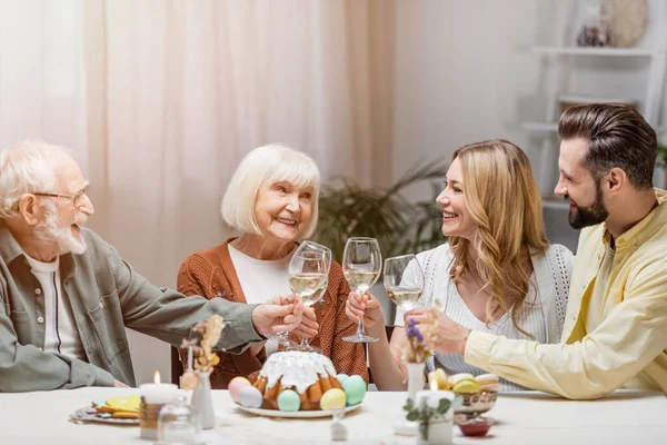 Glückliche Familie klimpert bei leckerem Osterkuchen und bemalten Eiern mit Weingläsern — Stockfoto