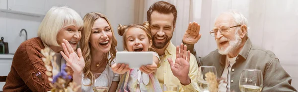 Familia emocionada agitando las manos durante la videollamada en el teléfono inteligente cerca de copas de vino, pancarta - foto de stock