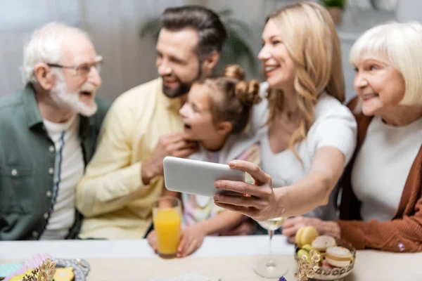 Mujer borrosa tomando selfie con la familia alegre durante la cena de Pascua - foto de stock