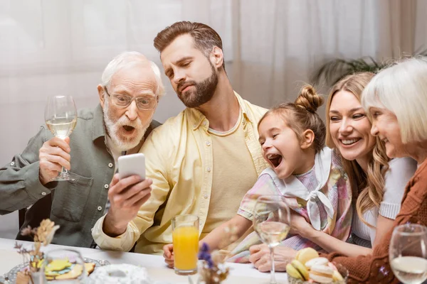 Uomo che mostra il telefono cellulare alla famiglia stupita durante la cena di Pasqua — Foto stock