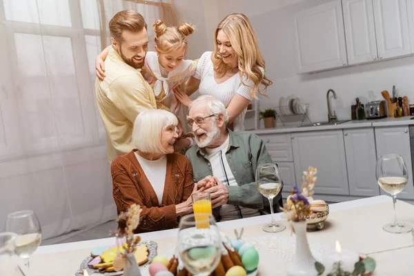 Feliz pareja de ancianos tomados de la mano durante la cena de Pascua con la familia - foto de stock