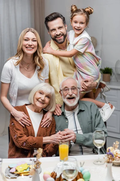 Família alegre olhando para a câmera perto da mesa com jantar de Páscoa — Fotografia de Stock