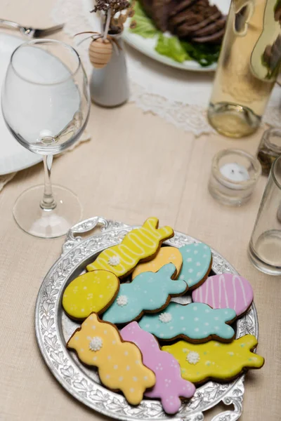 Vista de ángulo alto de las galletas de colores cerca de la botella de vino en la mesa servida para la cena de Pascua - foto de stock