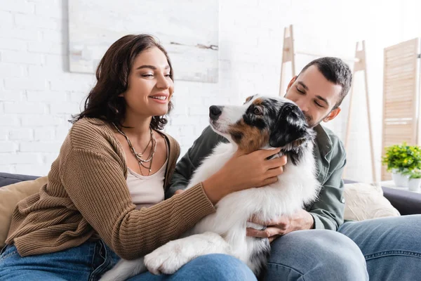Happy young woman cuddling australian shepherd dog near boyfriend — Stock Photo