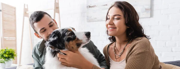 Happy young woman cuddling australian shepherd dog near boyfriend, banner — Stock Photo
