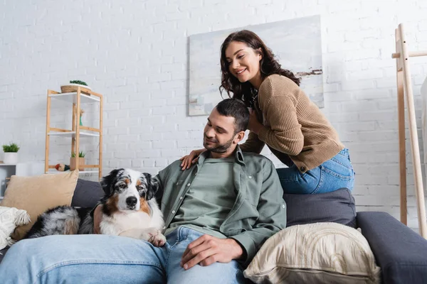 Sorridente giovane donna seduta vicino fidanzato barbuto e cane pastore australiano — Foto stock