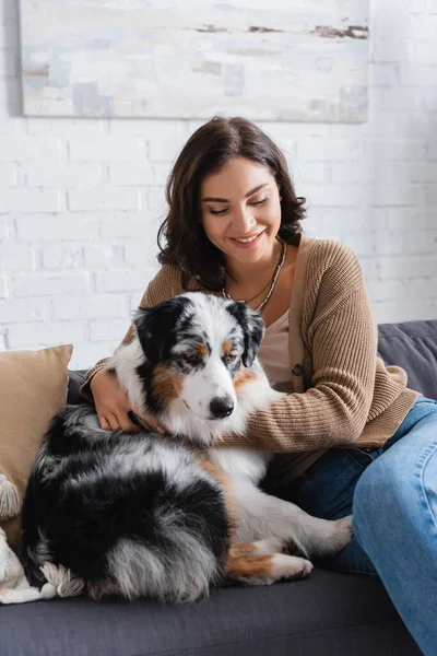 Happy woman cuddling australian shepherd dog while sitting on couch — Stock Photo