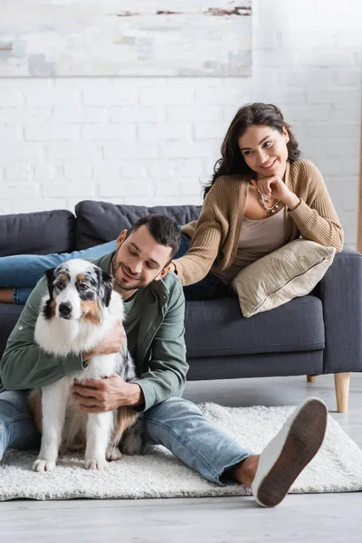 Happy bearded man cuddling australian shepherd dog near joyful girlfriend — Stock Photo