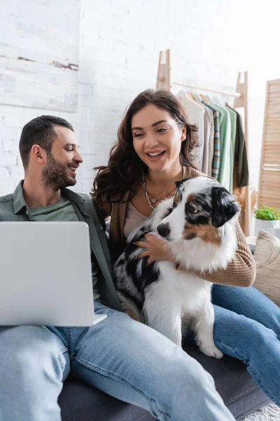 Happy young couple watching movie on laptop near australian shepherd dog — Stock Photo
