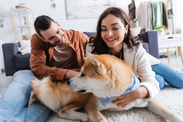 Young and cheerful couple cuddling akita inu dog in modern living room — Stock Photo