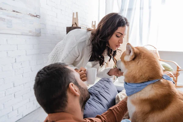 Bearded man looking at girlfriend with cup of coffee pouting lips near akita inu dog — Stock Photo