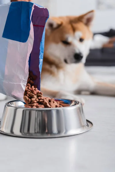 Packaging with pet food near bowl and blurred akita inu dog — Stock Photo