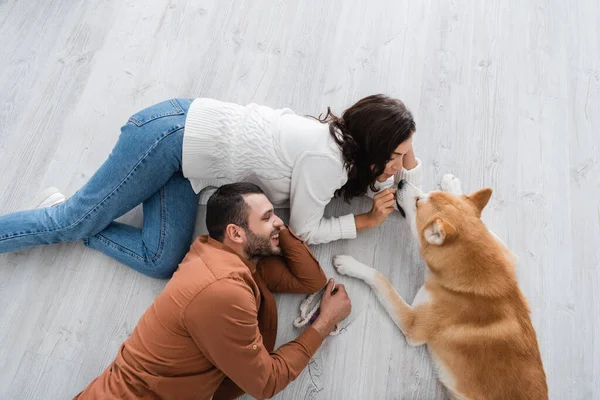 Top view of happy young couple lying of floor with akita inu dog — Stock Photo