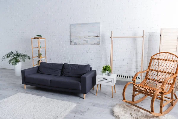 Moderna sala de estar con sofá, plantas verdes y mecedora de ratán - foto de stock
