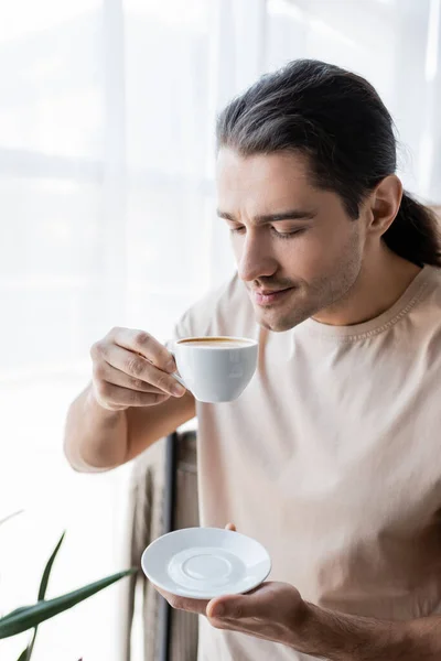 Homme aux cheveux longs tenant tasse de café et soucoupe — Photo de stock