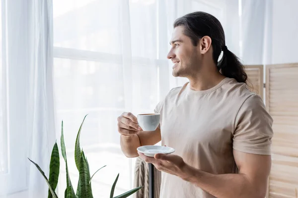 Счастливый мужчина с длинными волосами, держащий чашку кофе и блюдце — стоковое фото