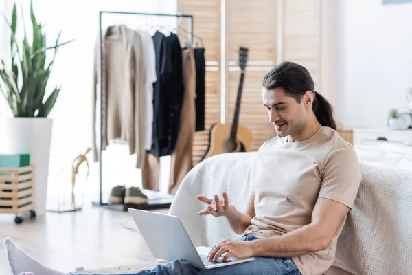 Sonriente hombre con el pelo largo gesto mientras se utiliza el ordenador portátil - foto de stock