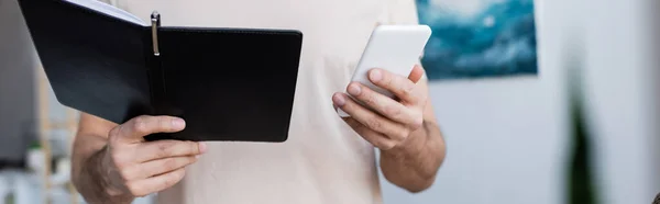 Vista cortada do homem segurando telefone celular e notebook em casa, banner — Fotografia de Stock