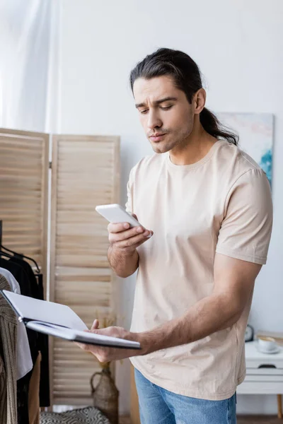 Чоловік тримає мобільний телефон і блокнот вдома — Stock Photo