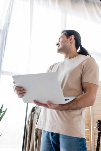 Blick auf einen lächelnden Mann mit langen Haaren, der einen Laptop hält — Stockfoto