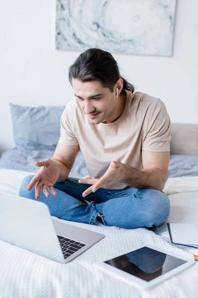 Mann mit Kopfhörer gestikuliert bei Videoanruf im Bett — Stockfoto