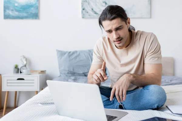 Mann mit Kopfhörer gestikuliert bei Videoanruf im Schlafzimmer — Stockfoto