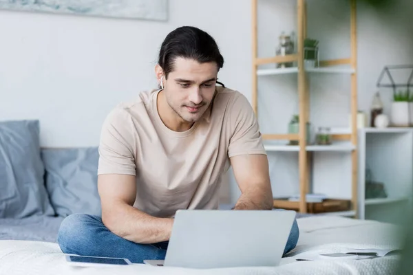 Mann mit Kopfhörer benutzt Laptop im Schlafzimmer — Stockfoto