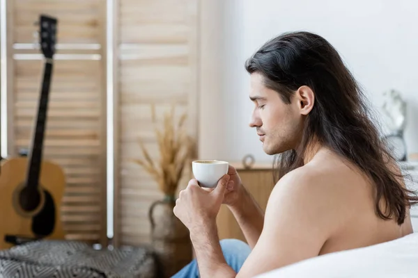 Vista laterale dell'uomo senza maglietta con i capelli lunghi che tengono la tazza di caffè — Foto stock