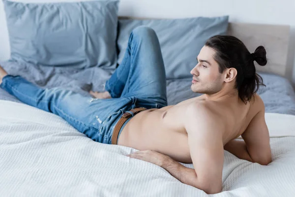 Shirtless man in blue jeans lying on bed at home — Stock Photo