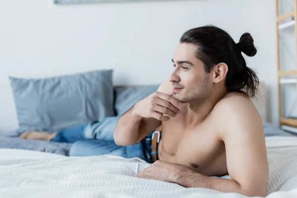 Homem sorridente e sem camisa de jeans azul deitado na cama em casa — Fotografia de Stock