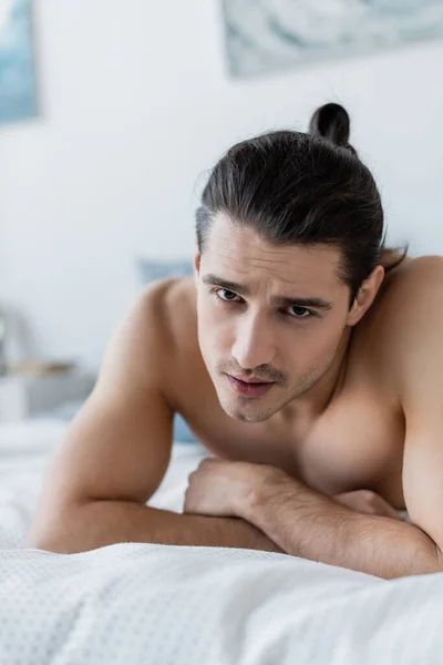 Shirtless man looking at camera while lying on bed — Stock Photo