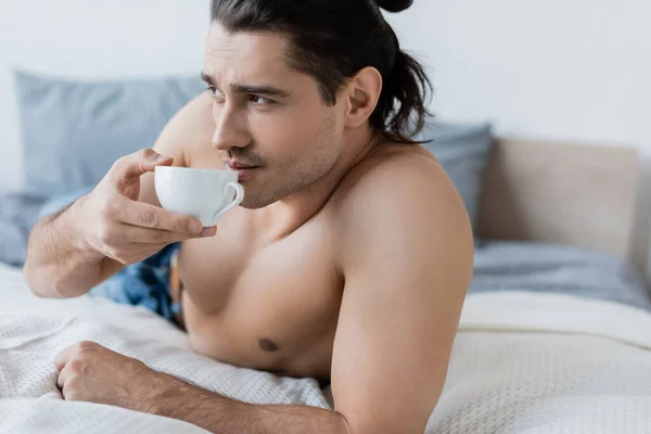 Hemdloser Mann trinkt Kaffee, während er Tasse im Schlafzimmer hält — Stockfoto